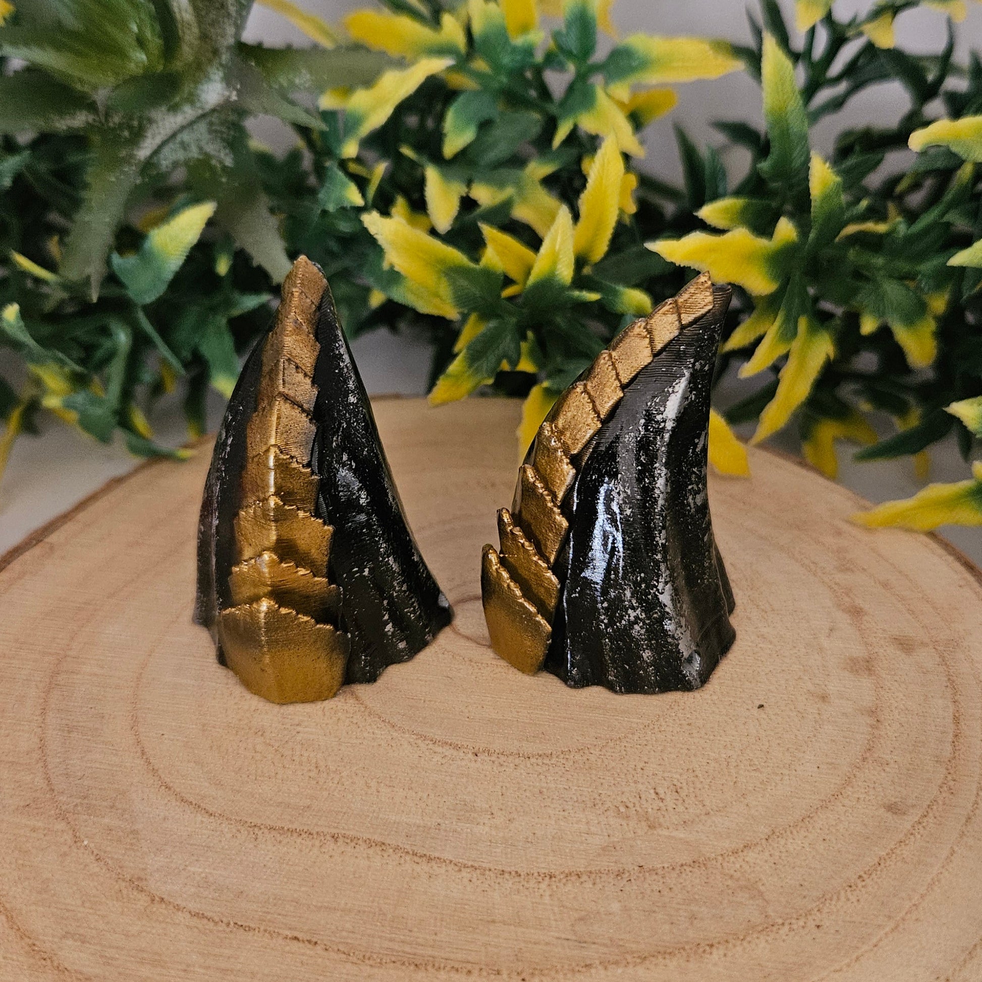 Handbemalte 3D-gedruckte Cosplay-Hörner aus PLA in Schwarz-Gold auf Holzdisplay, präsentiert mit dekorativer Pflanze – Fantasy-Accessoire für LARP, Halloween und Kostüm.