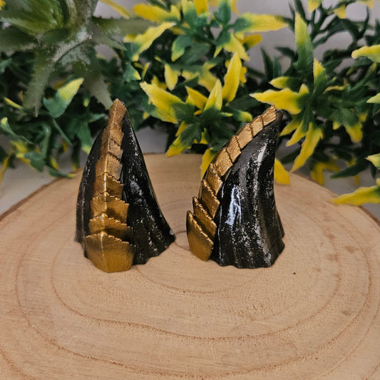 Handbemalte 3D-gedruckte Cosplay-Hörner aus PLA in Schwarz-Gold auf Holzdisplay, präsentiert mit dekorativer Pflanze – Fantasy-Accessoire für LARP, Halloween und Kostüm.